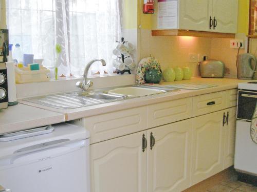 Thorpe MarketにあるPuddleduck Cottageの白いキャビネット、シンク、食器洗い機付きのキッチンが備わります。