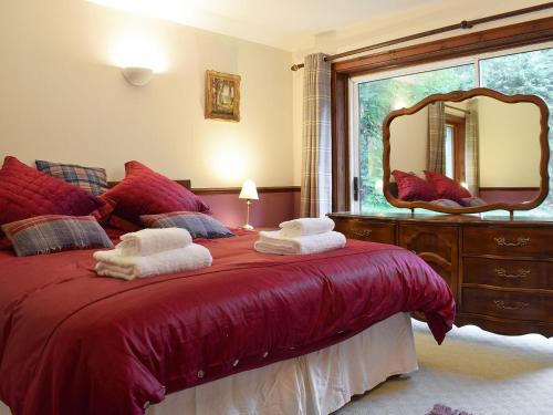 a bedroom with a red bed with a large mirror at Drummond Cottage in Kenmore