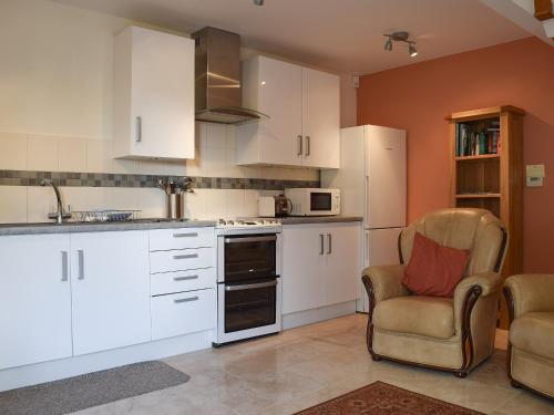 a kitchen with white cabinets and a chair and a microwave at Camelia Cottage in Witney