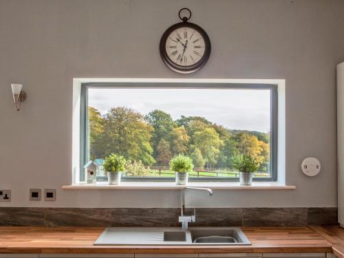 a kitchen window with a sink and a clock at Three The Old Stables in Knitsley