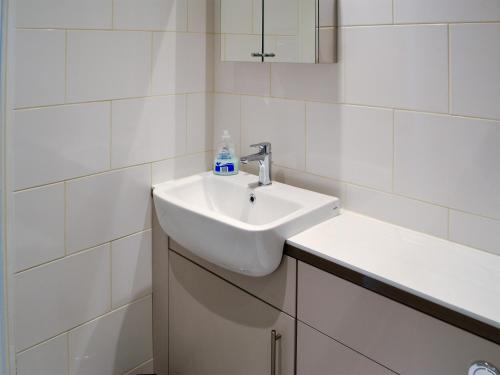 a white sink in a bathroom with white tiles at Oake Cottage in Warkworth