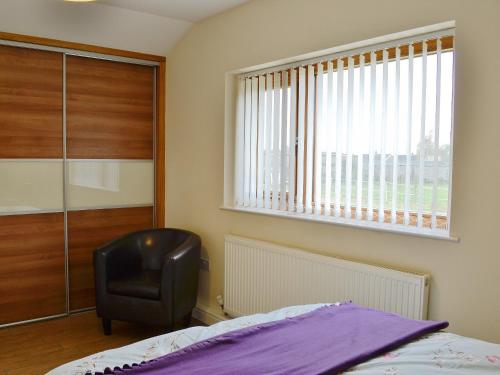 a bedroom with a bed and a chair and a window at Hawthorne Cottage in Winthorpe