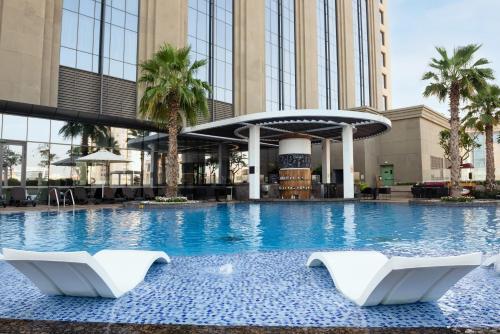 a swimming pool with two white chairs in front of a building at Hyatt Regency Dubai Creek Heights in Dubai