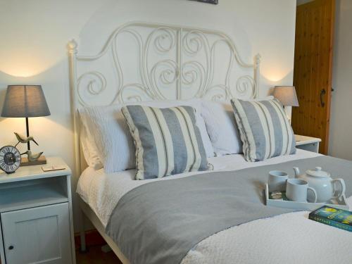 a white bed with pillows and a table with a clock at Birdsong Cottage in Hartland
