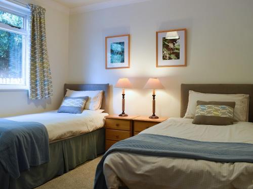 two beds in a bedroom with two lamps and a window at Glebe Cottage in New Scone