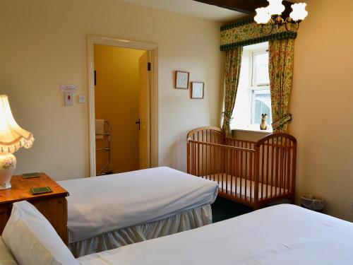 a bedroom with two beds and a window and a crib at Busy Lizzie Cottage-mfo in Akeld