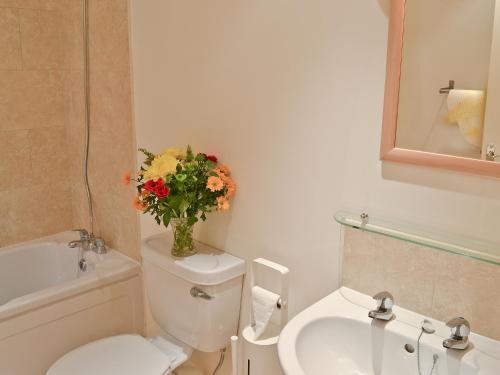 a bathroom with a toilet and a sink and a vase of flowers at The Cobbles in West Pennard