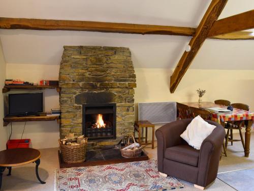 a living room with a stone fireplace and a chair at Erw Goed Hen Stabl in Arthog