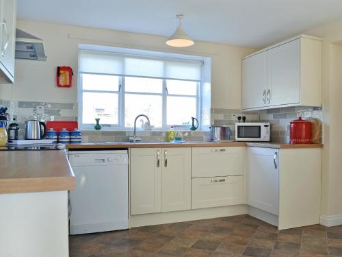 a kitchen with white cabinets and a sink and a microwave at Manor Cottage in Old Byland