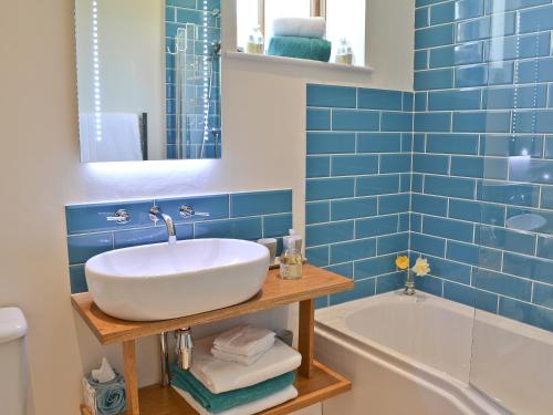a blue tiled bathroom with a sink and a tub at Fig Cottage in Brabourne