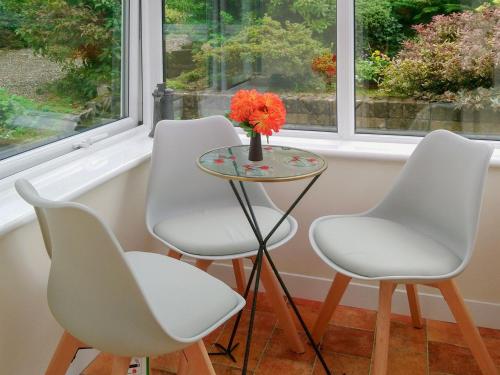 three white chairs and a table with a vase of flowers at Briar Bank Bungalow in Cockermouth