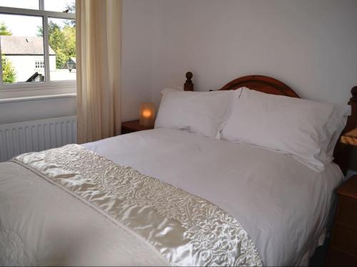 uma cama com lençóis e almofadas brancos e uma janela em Church Walk Cottage em Kendal