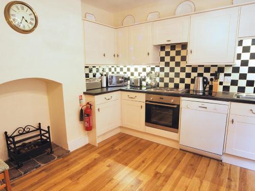 a kitchen with white cabinets and a clock on the wall at Berwyn Stationmasters House - Hw7641 in Llangollen