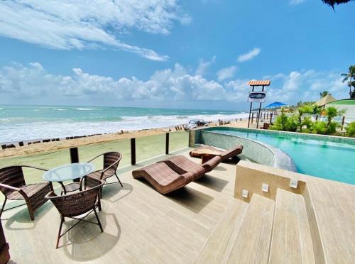 a swimming pool with chairs and a table and the beach at Pousada Maracabana Spa in Porto De Galinhas