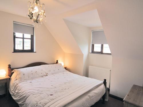 a bedroom with a bed with a chandelier and two windows at Pebble Cottage - Hw7447 in Broad Haven