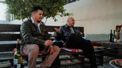 two men sitting on a bench with wine bottles at Cabaña R y A Valle de Guadalupe in Valle de Guadalupe