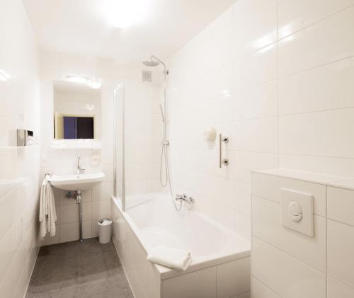 a white bathroom with a tub and a sink at Hotel Dordrecht in Dordrecht