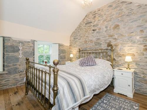 a bedroom with a bed and a stone wall at Waterfall Wood Cottage in Patterdale
