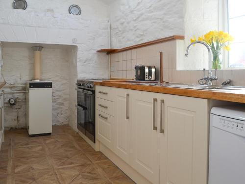 a kitchen with white cabinets and a sink at Porth Cormon Farmhouse in Llangwnadl