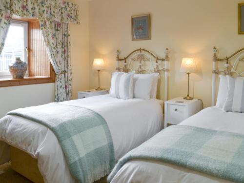 a bedroom with two beds and two lamps and a window at Hazels Cottage in Kilchenzie