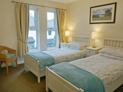 a bedroom with two beds and a chair and two windows at Badger Cottage in Ambleside