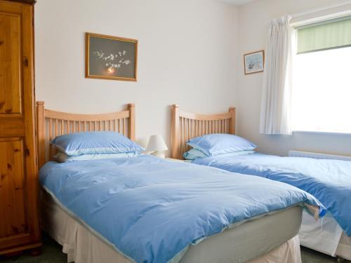 two beds in a bedroom with blue sheets and a window at Craigneish Bungalow in Trearddur