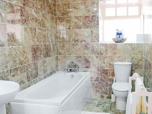 a bathroom with a tub and a toilet and a sink at Stable Cottage in Burythorpe