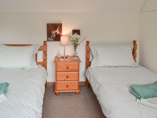 a bedroom with two twin beds and a nightstand with flowers on it at Henley Bridge Holiday Cottage in Ashburnham