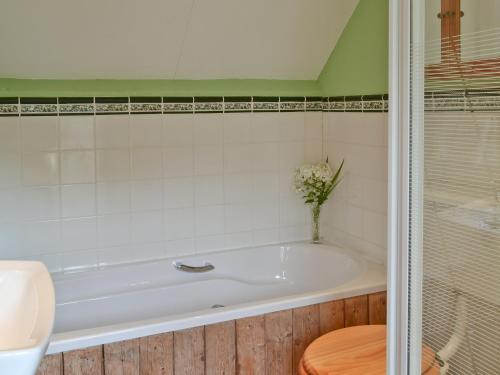 a bath tub with a vase of flowers in a bathroom at Henley Bridge Holiday Cottage in Ashburnham