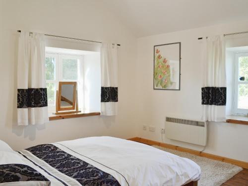 a white bedroom with a bed and two windows at The Old Granary in Ballindalloch