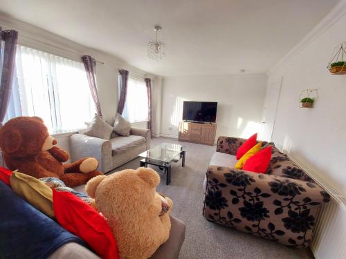 Dois ursos de peluche sentados num sofá na sala de estar. em Teddy Bears' 3-bedroom Maisonette em Saltcoats