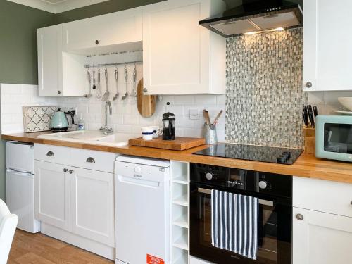 Sea PallingにあるField Crestの白いキャビネットと黒い食器洗い機付きのキッチンが備わります。