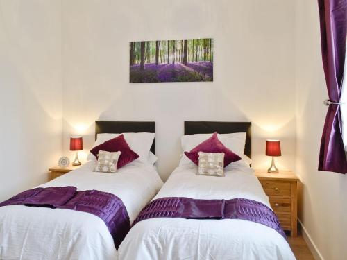 two beds in a bedroom with purple pillows at Rose Cottage - 28176 in Fairgirth