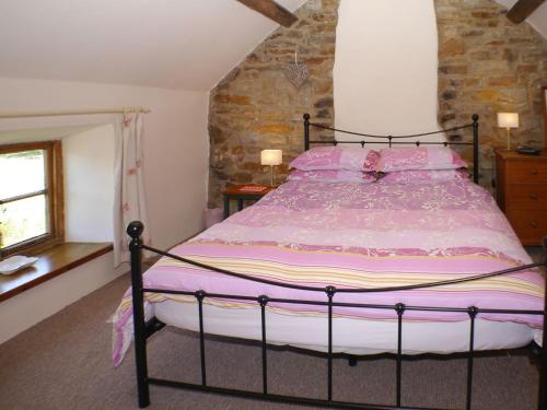 a bedroom with a large bed with pink sheets at Garden Cottage in Onecote