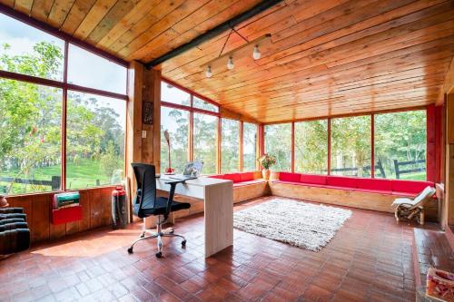 an office with a red couch and a desk in a room with windows at Cabaña de Hacienda Nebraska in Zipacón