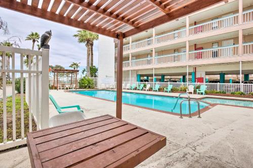 a pool with a wooden table and chairs next to a building at Oceanfront Corpus Christi Condo with Pool! in Corpus Christi