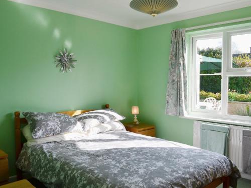 a green bedroom with a bed and a window at Corney Grain in Teversham