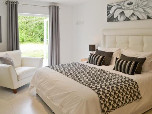a white bedroom with a large bed and a chair at Honey Pippin in Cheriton Bishop