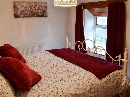 - une chambre avec un lit doté d'oreillers rouges et une fenêtre dans l'établissement Wild Flower Cottage, à Youlgreave