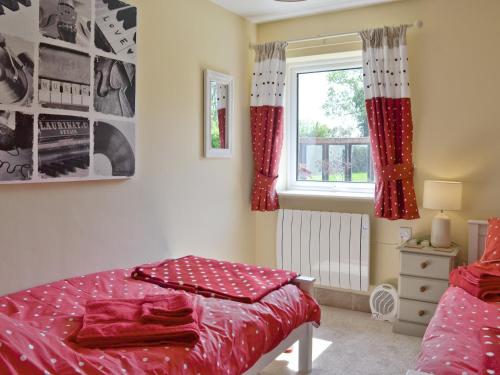 a bedroom with a bed with red sheets and a window at Mill Cottage in Stillington