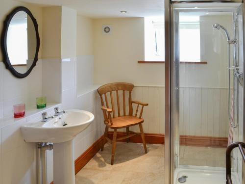 a bathroom with a sink and a chair next to a shower at Cobweb Cottage in Elsdon