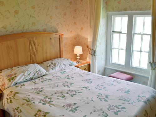 a bedroom with a bed with a floral bedspread and a window at Isfryn in Llanystumdwy