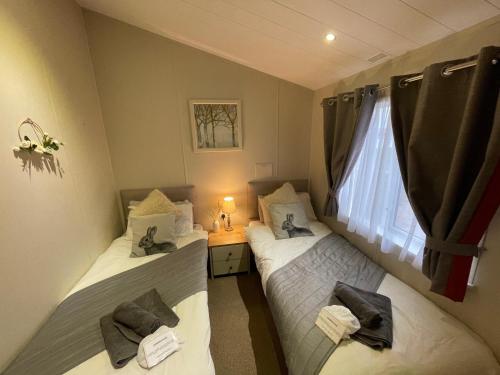 two twin beds in a room with a window at Indulgence lakeside lodge i1 with hot tub, private fishing peg situated at Tattershall Lakes Country Park in Tattershall