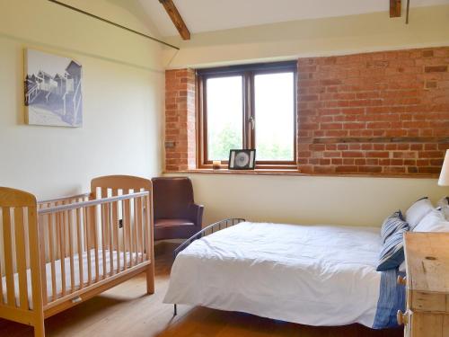 a bedroom with a crib and a brick wall at Partridge Barn in Sculthorpe
