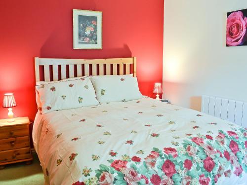 a red bedroom with a bed with a floral bedspread at The Stables At Old Vicarage Cottage in Abergele