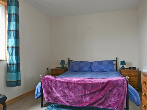 a bedroom with a bed with a purple blanket on it at Bute Cottage in Daliburgh