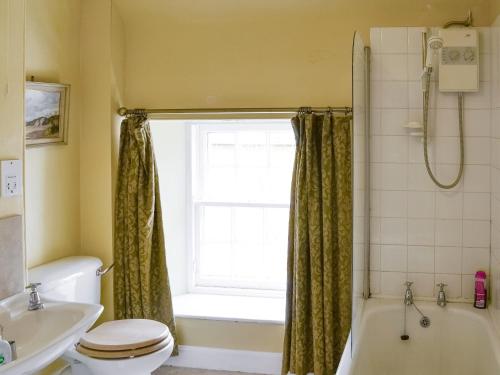 a bathroom with a tub and a toilet and a window at Lochside Garden House - S4484 in Town Yetholm