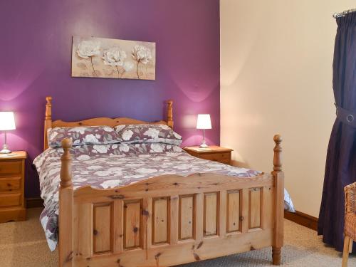 a bedroom with a wooden bed with purple walls at Beudy Mawr - 16985 in Brynsiencyn