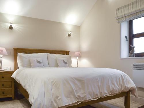 a bedroom with a large bed with white sheets and a window at Curlew Barn in Middleham