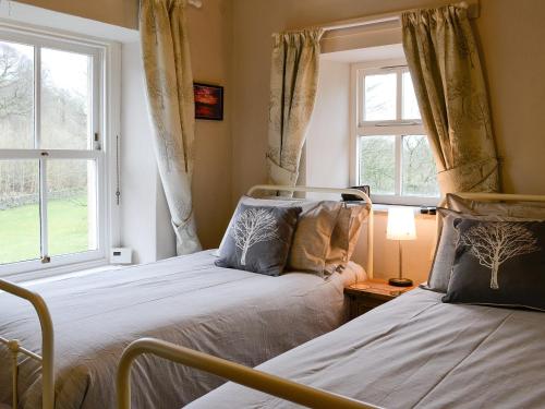 two beds in a room with two windows at Miller Cottage in Malham